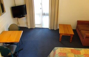 Quarto com cama, escrivaninha, cadeira, televisão e sofá.