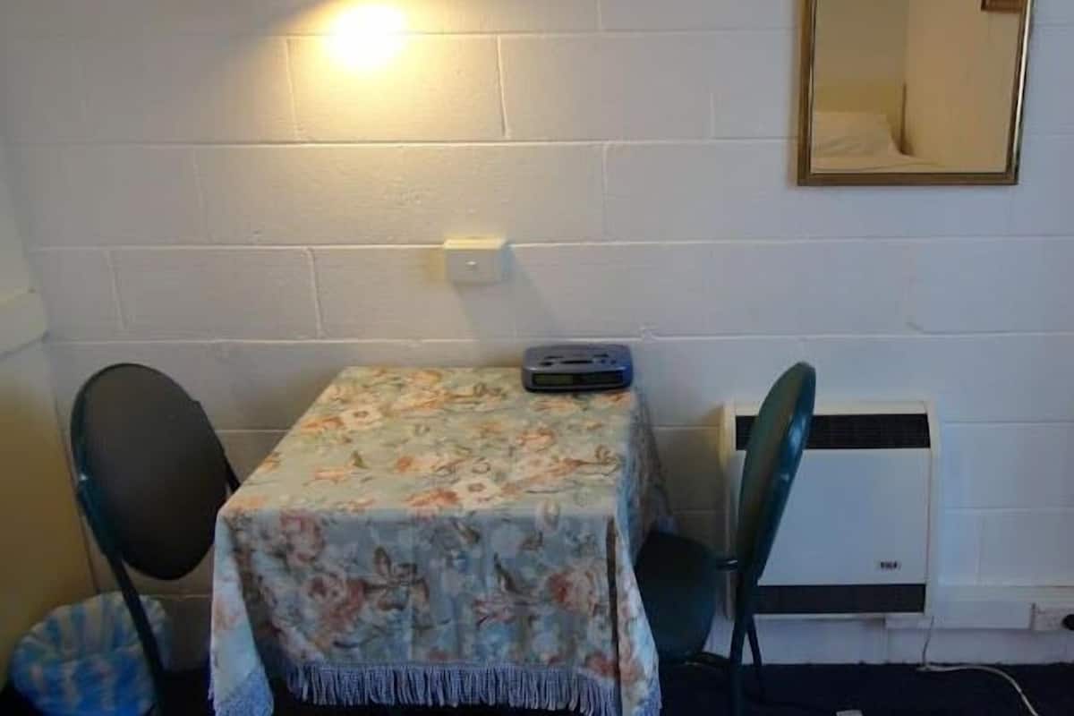 A small room with a table covered by a floral tablecloth, a chair, a heater, and a mirror on the wall.