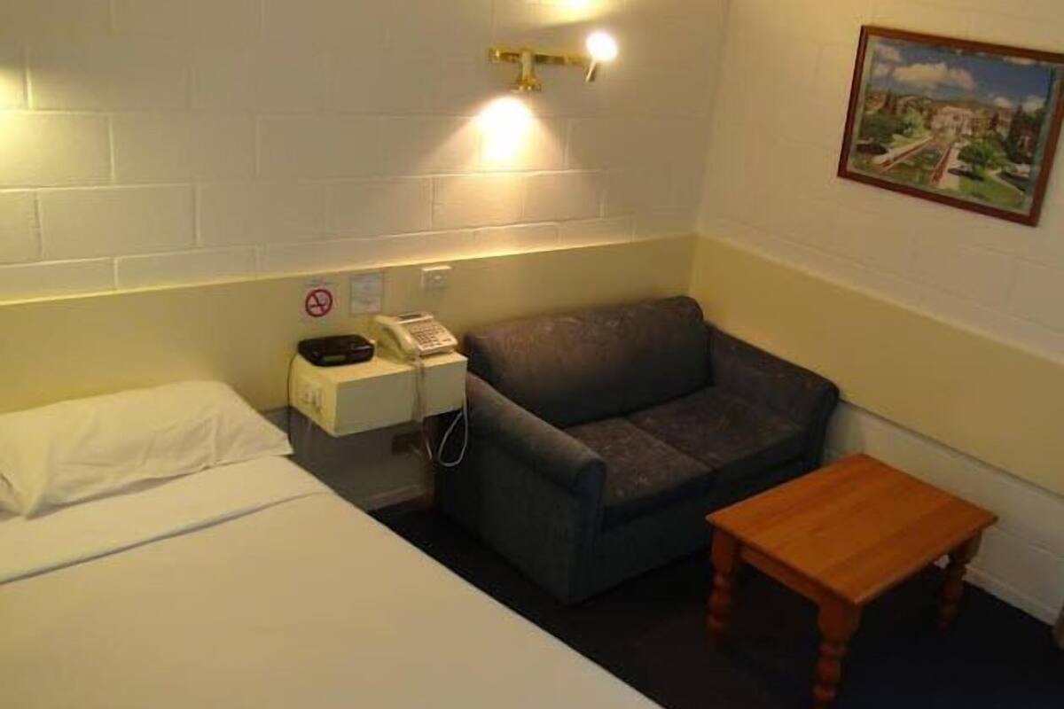 A small room with a bed, a couch, a wooden table, a telephone, and a wall-mounted light fixture.