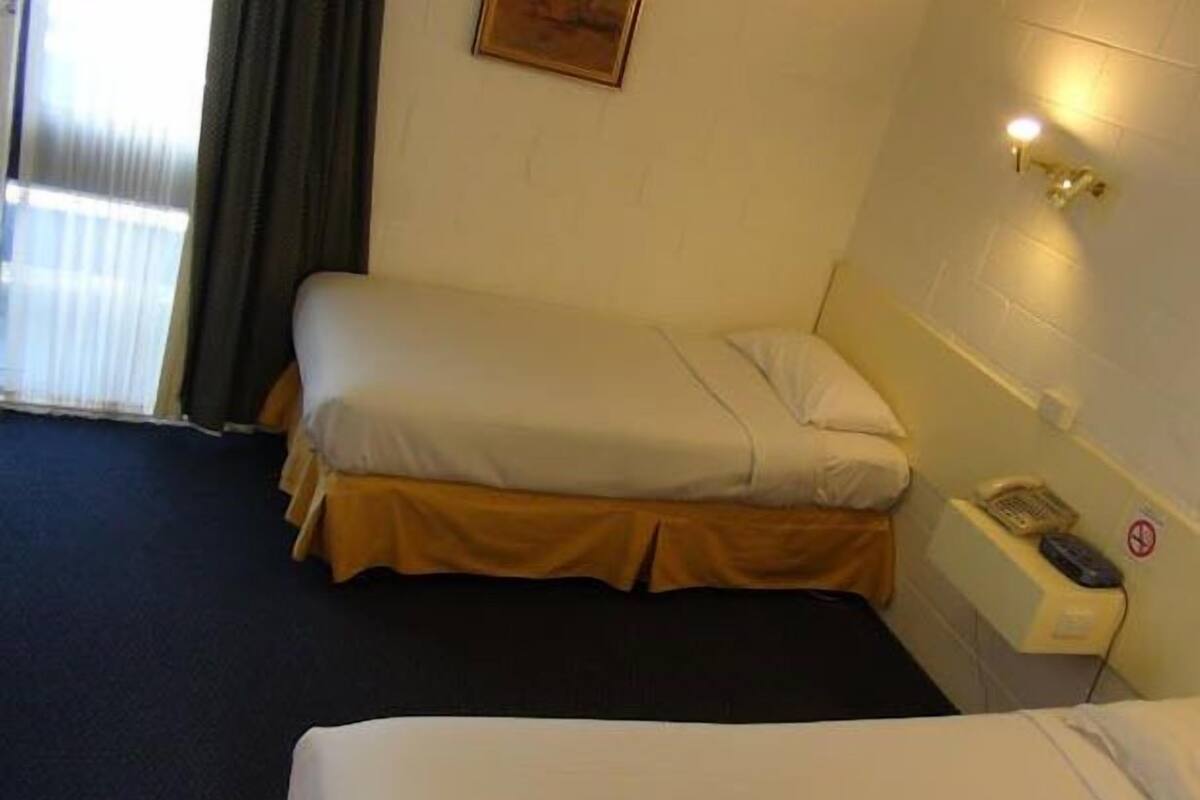 A hotel room with a single bed, a bedside table with a phone, and a window with curtains.