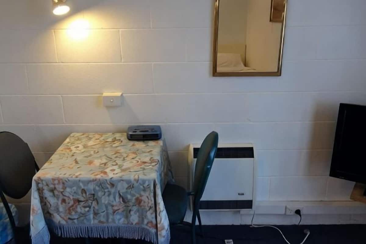 A small room with a table, a chair, a heater, a mirror, and a television.