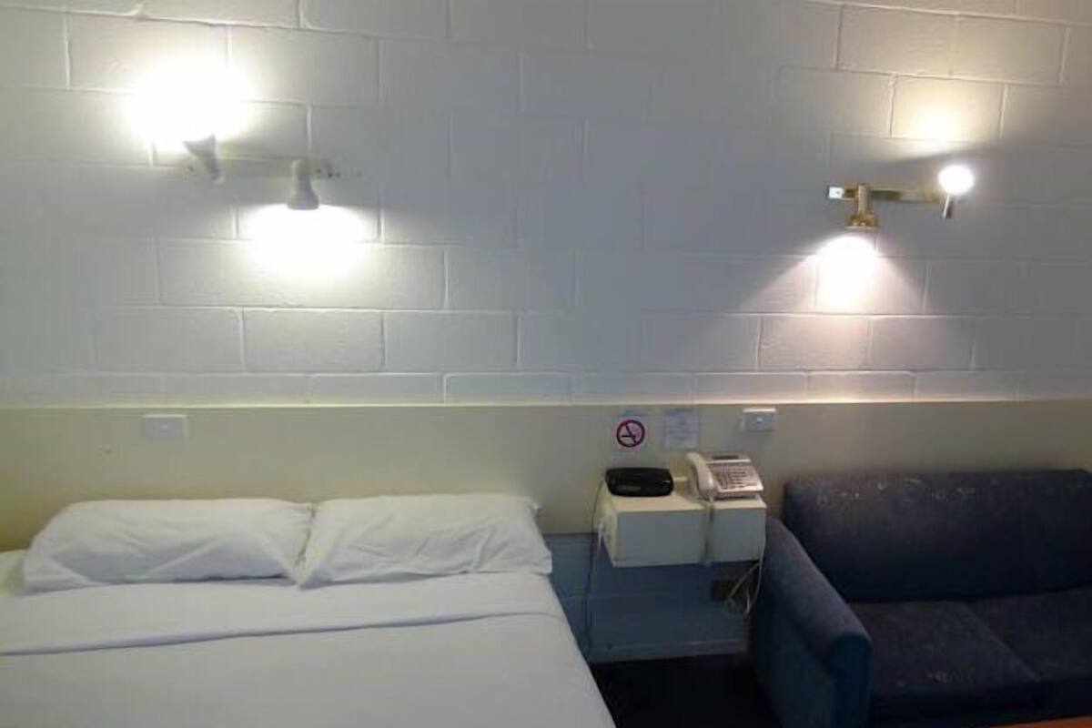 A hotel room with a bed, a nightstand, a phone, and a couch.