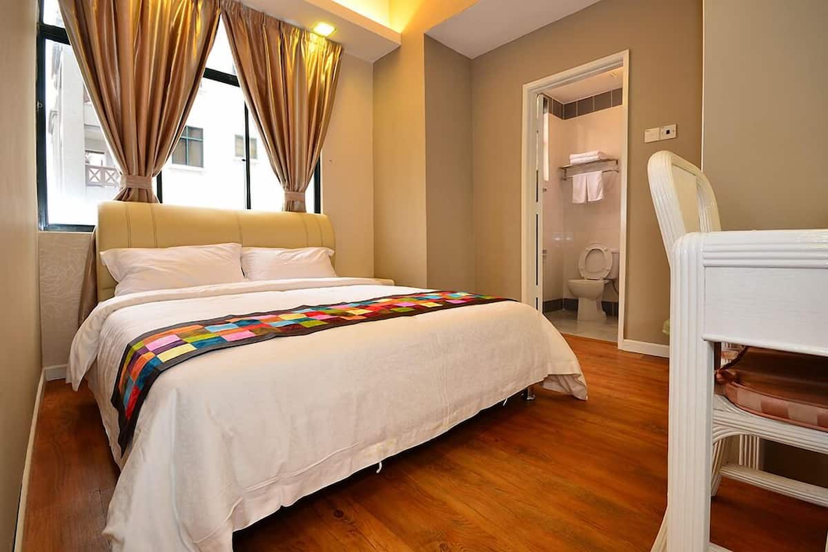 A bedroom with a bed, a bedside table, a chair, and a bathroom visible through an open door.