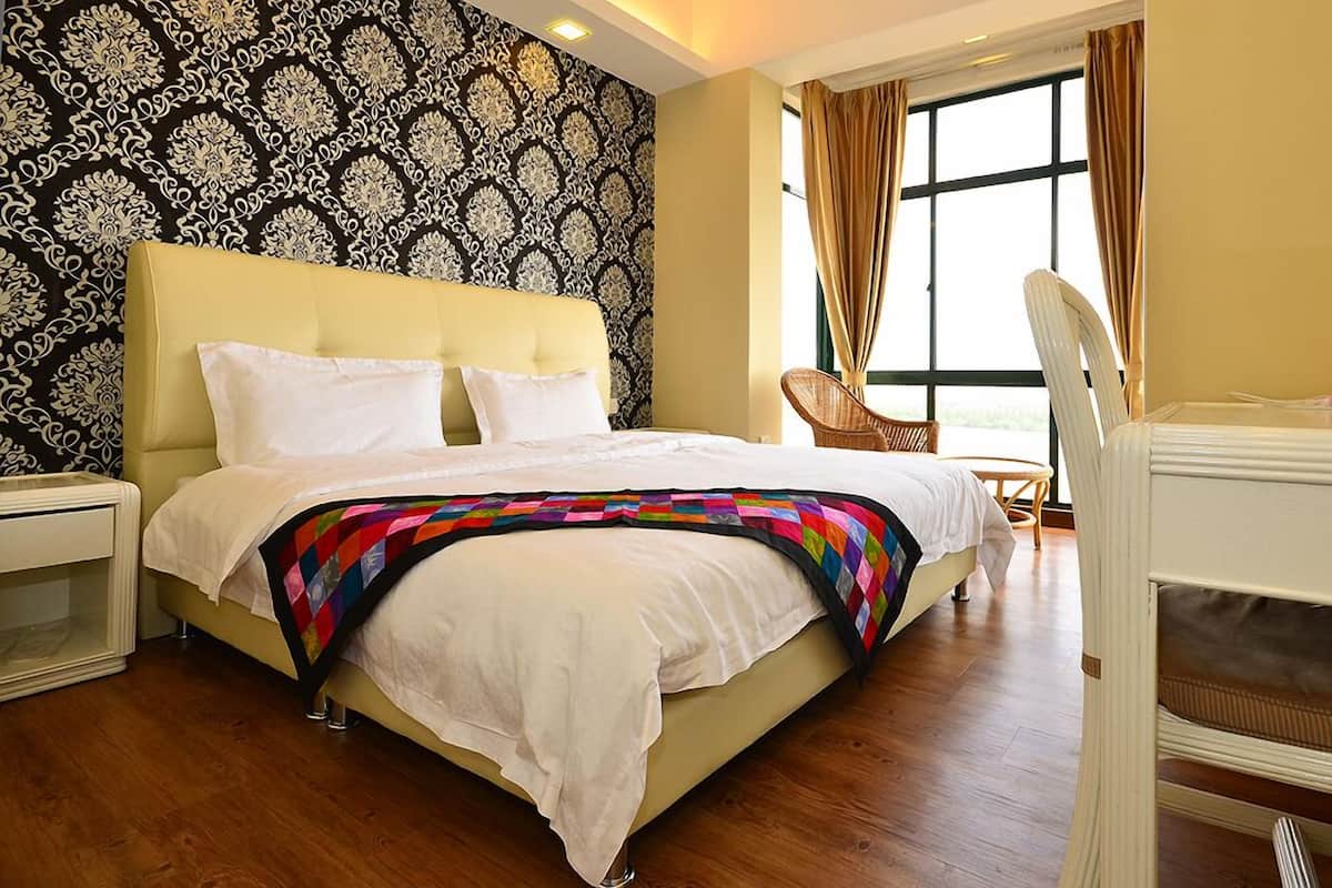 A hotel room with a large bed, a bedside table, a chair, and a window with curtains.