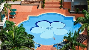 Una piscina con diseño floral, rodeada de palmeras y sillones de descanso.