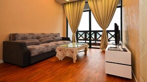 Una sala de estar con sofá, una mesa de centro de vidrio, mueble para televisor y un balcón con cortinas.