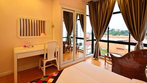 Habitación de hotel con cama, escritorio y silla, una mesita y balcón con cortinas.