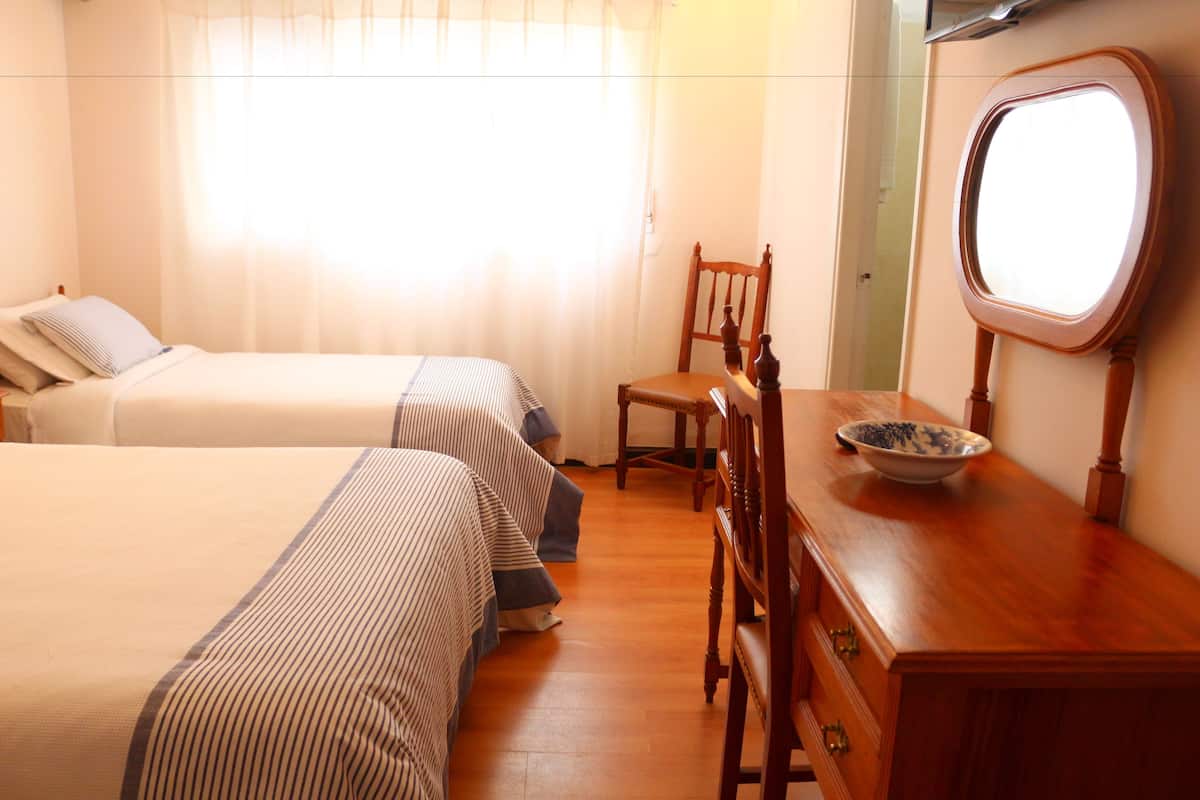 A hotel room with two beds, a wooden dresser, a chair, and a mirror.