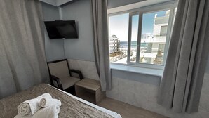 A hotel room with a bed, a small table, a chair, a TV mounted on the wall, and a window with a view of buildings and the sea. - Hotel Playa Brava (Punta del Este)