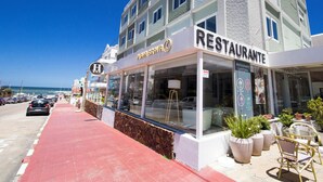 A restaurant with a red pedestrian walkway, outdoor seating with potted plants, and a view of the ocean. - Hotel Playa Brava (Punta del Este)
