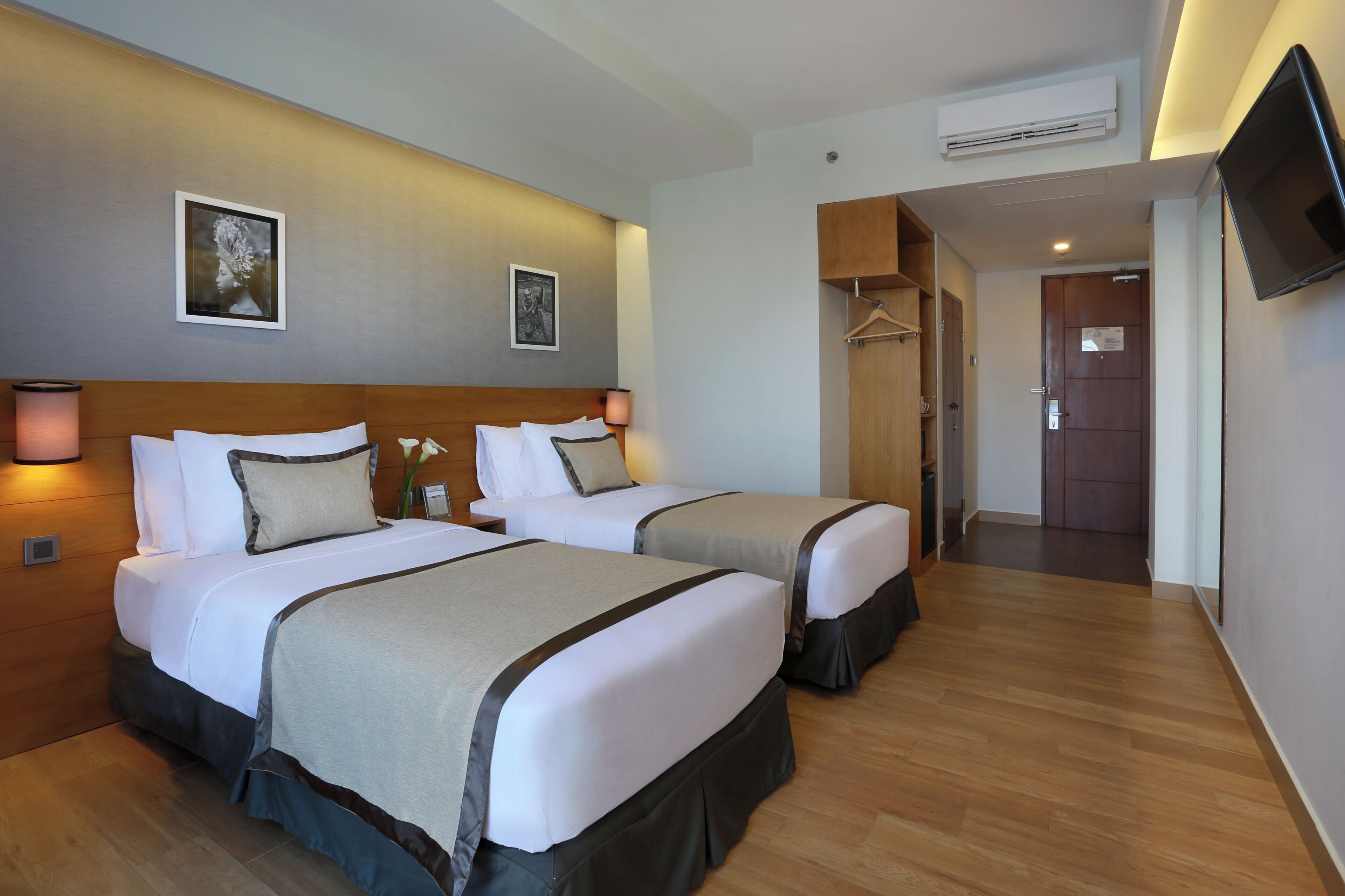 Une chambre d’hôtel avec deux lits, une tête de lit en bois, des œuvres d’art accrochées au mur, une télévision et un plancher en bois.