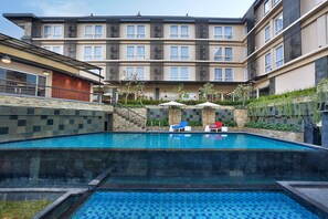 A swimming pool with lounge chairs and umbrellas, surrounded by a building with multiple floors and balconies. - Azana Boutique Hotel Denpasar (Denpasar)