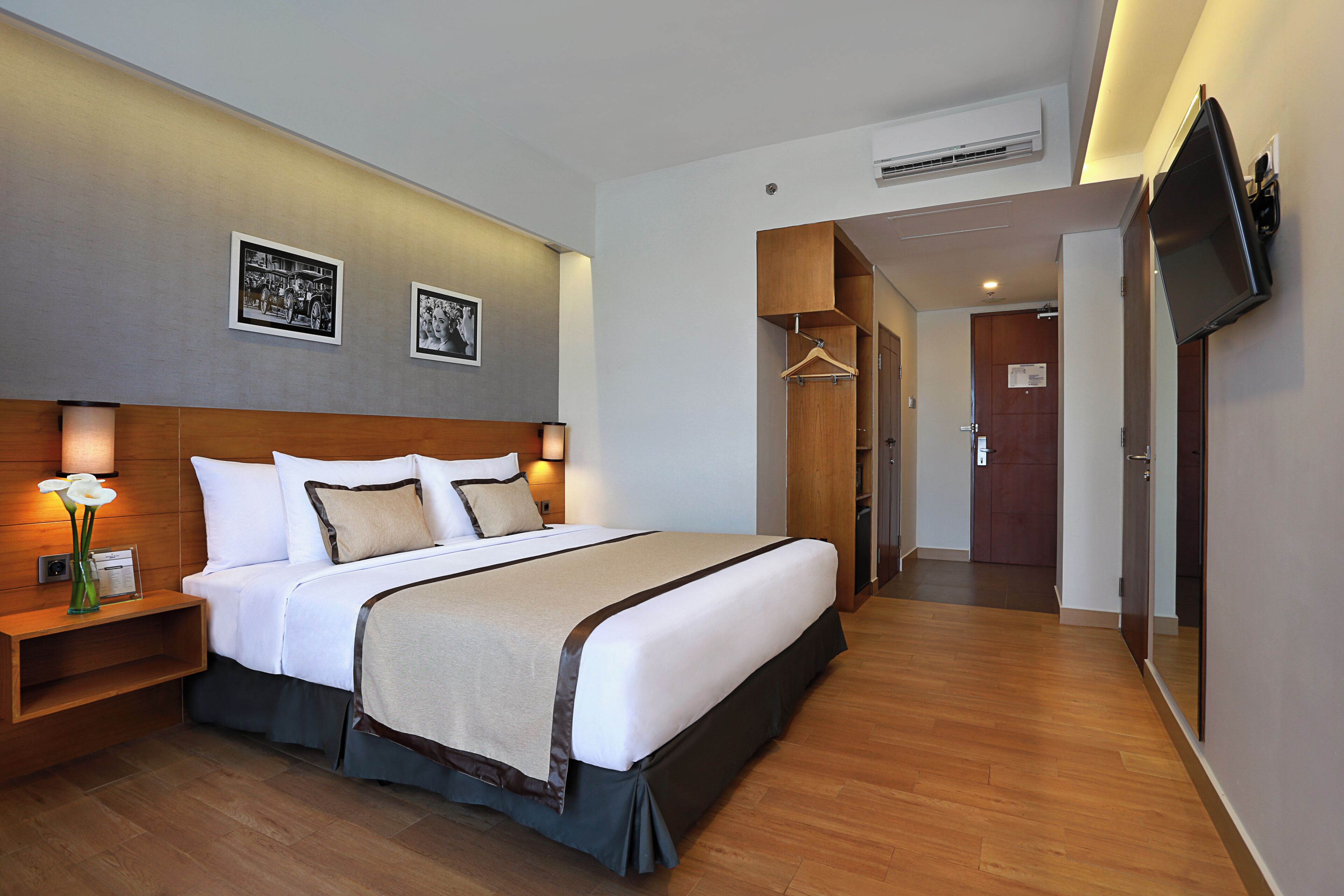 A hotel room with a large bed, bedside tables, a TV mounted on the wall, and a wooden floor.