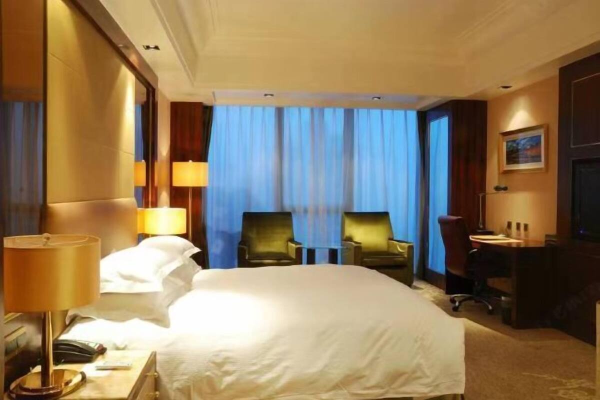A hotel room with a large bed, two armchairs, a desk, and a lamp.