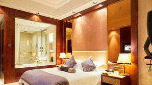 A hotel room with a large bed, bedside lamps, a nightstand, a mirror, and a television.