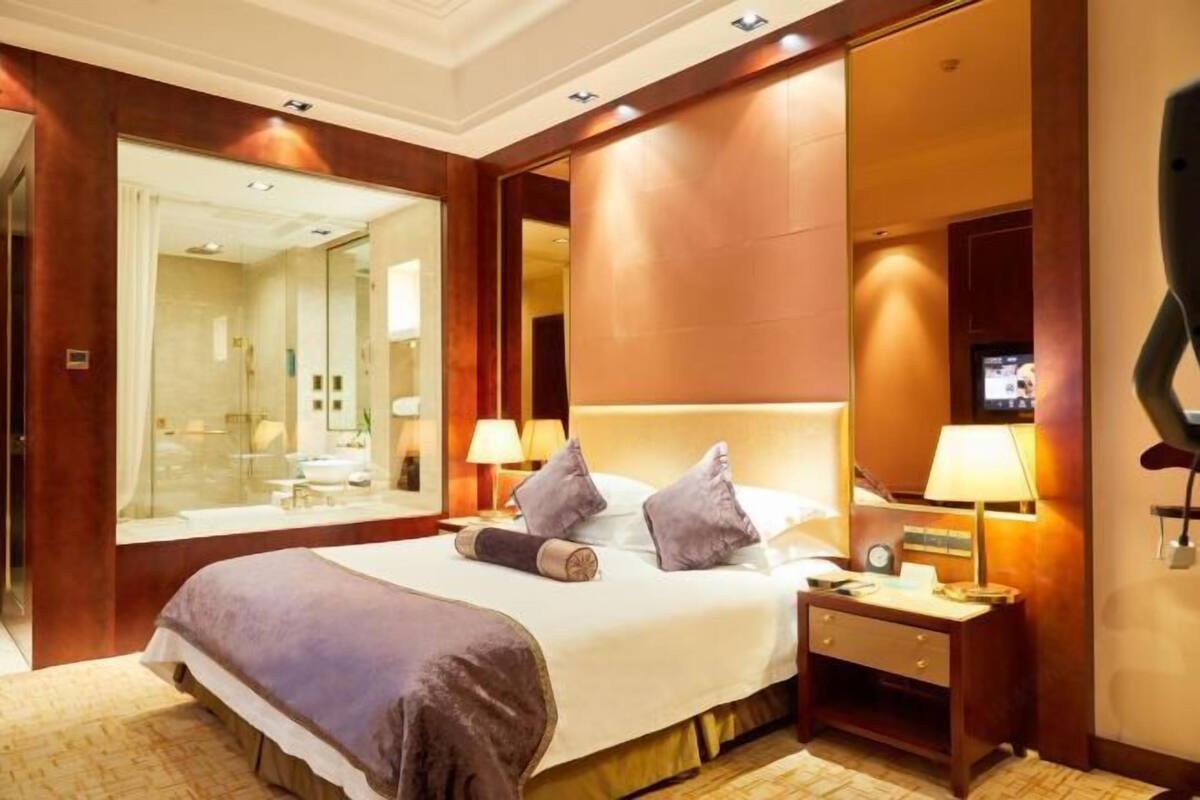 A hotel room with a large bed, bedside lamps, a nightstand, a mirror, and a television.