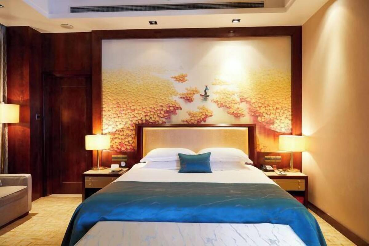 A hotel room with a large bed, two bedside tables, a nightstand, a lamp, and a wall mural.