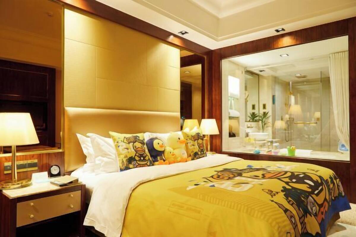 A hotel room with a large bed, a nightstand with a lamp, a mirror, and a view of the bathroom.