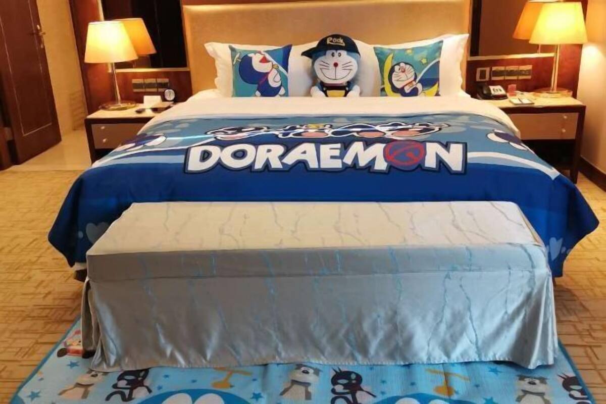 A hotel room with a bed featuring Doraemon-themed bedding and pillows.