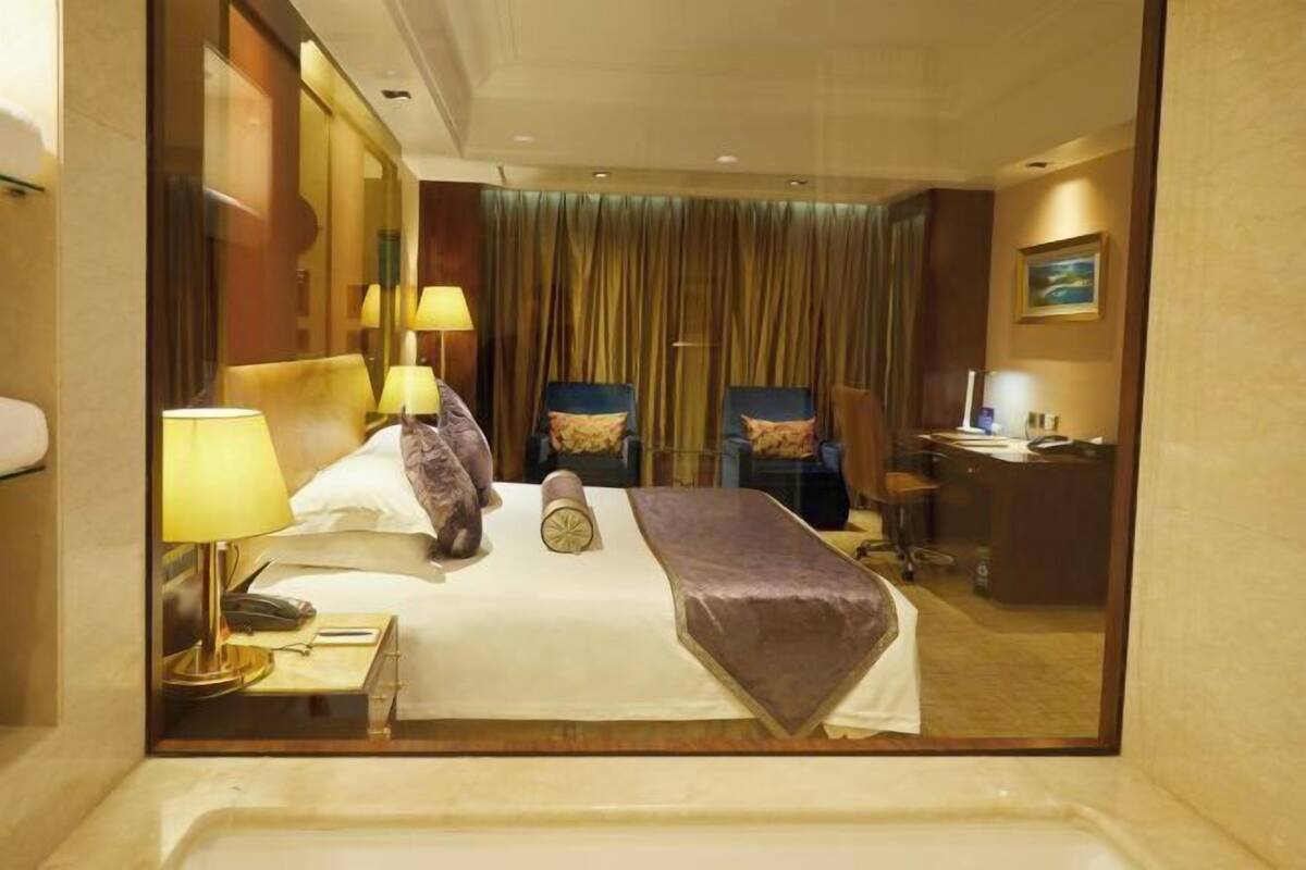 A hotel room with a bed, two chairs, a desk, and a mirror.