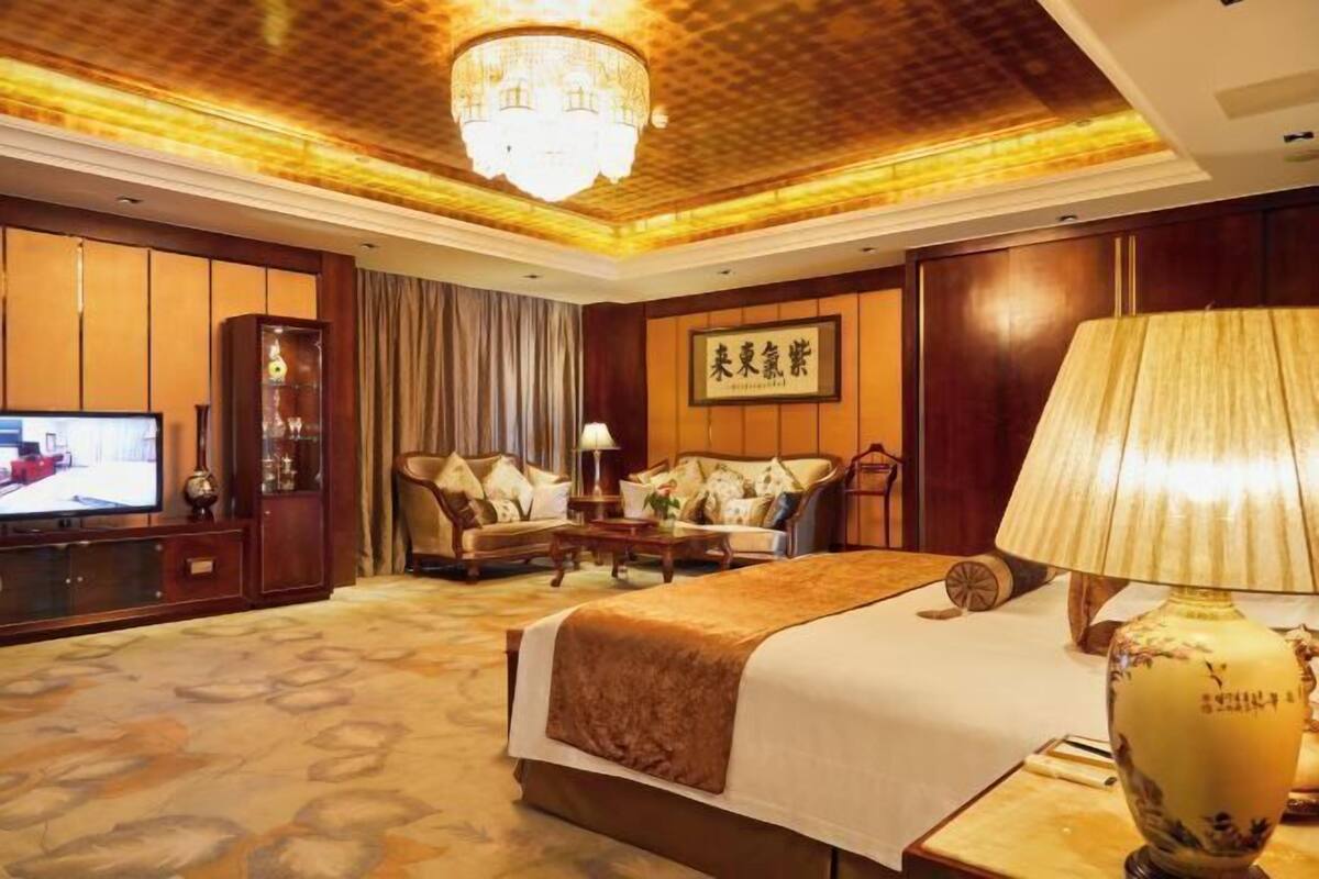 A hotel room with a large bed, a television, a sofa, and a chandelier.