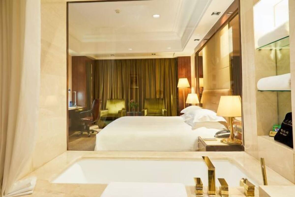 A hotel room with a large bed, a desk, a chair, a desk lamp, and a mirror.