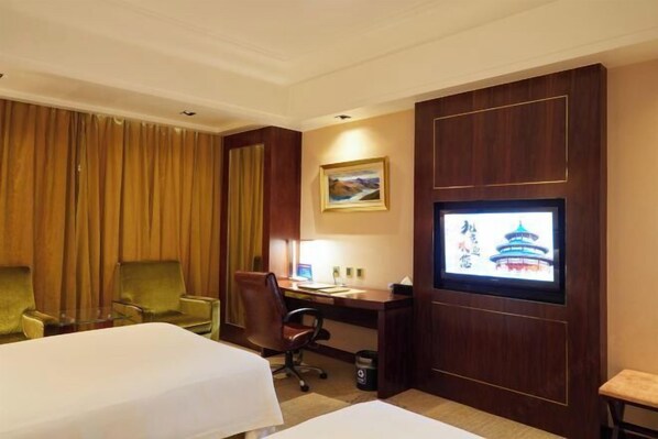 A hotel room with two beds, a desk with a computer, a chair, and a TV on the wall.