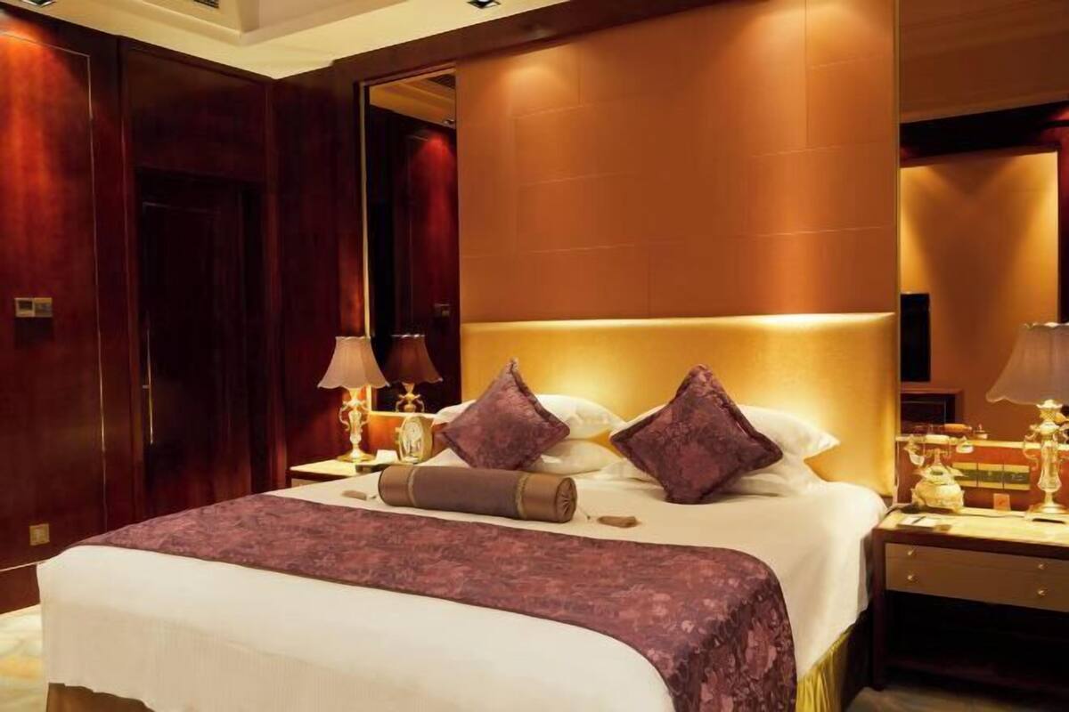 A hotel room with a large bed, wooden paneling, a nightstand with a lamp, and a mirror.