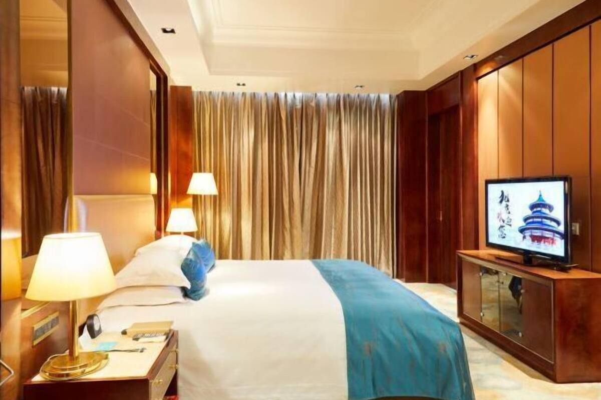 A hotel room with a bed, two bedside lamps, a television on a wooden cabinet, and a curtain backdrop.