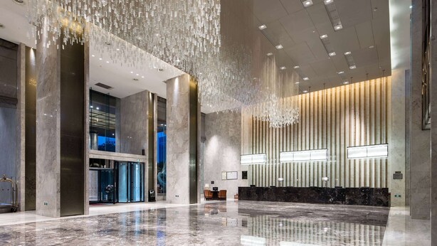 Un hall d’entrée spacieux, doté d’un sol en marbre poli, d’un comptoir de réception et d’un lustre moderne.