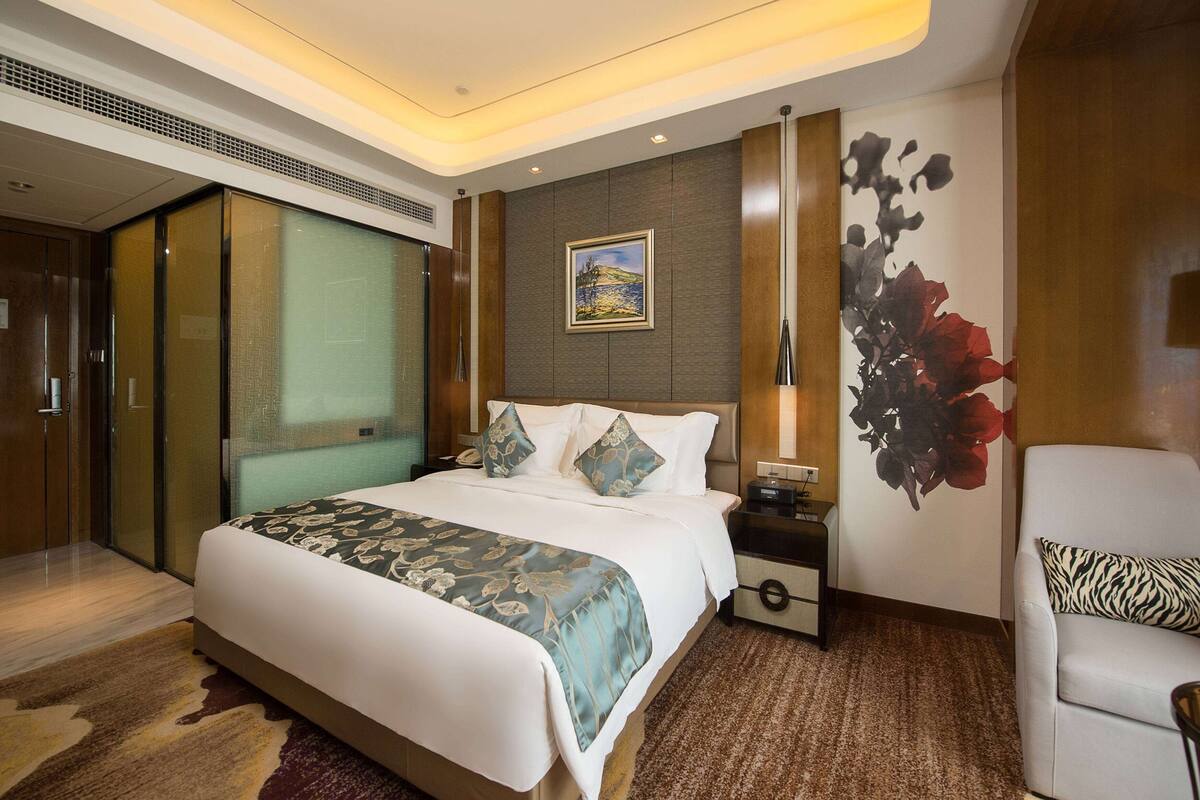 Ein Hotelzimmer mit einem großen Bett, einem Nachttisch, einem Sessel, einem Wandbild und einer Schiebetür.