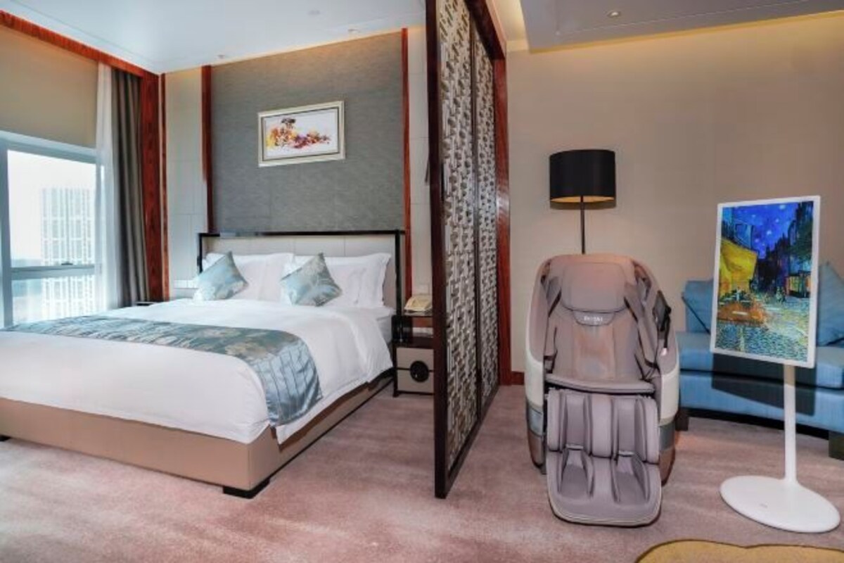 Ett hotellrum med en säng, en massagefåtölj, en tavla och utsikt över staden.