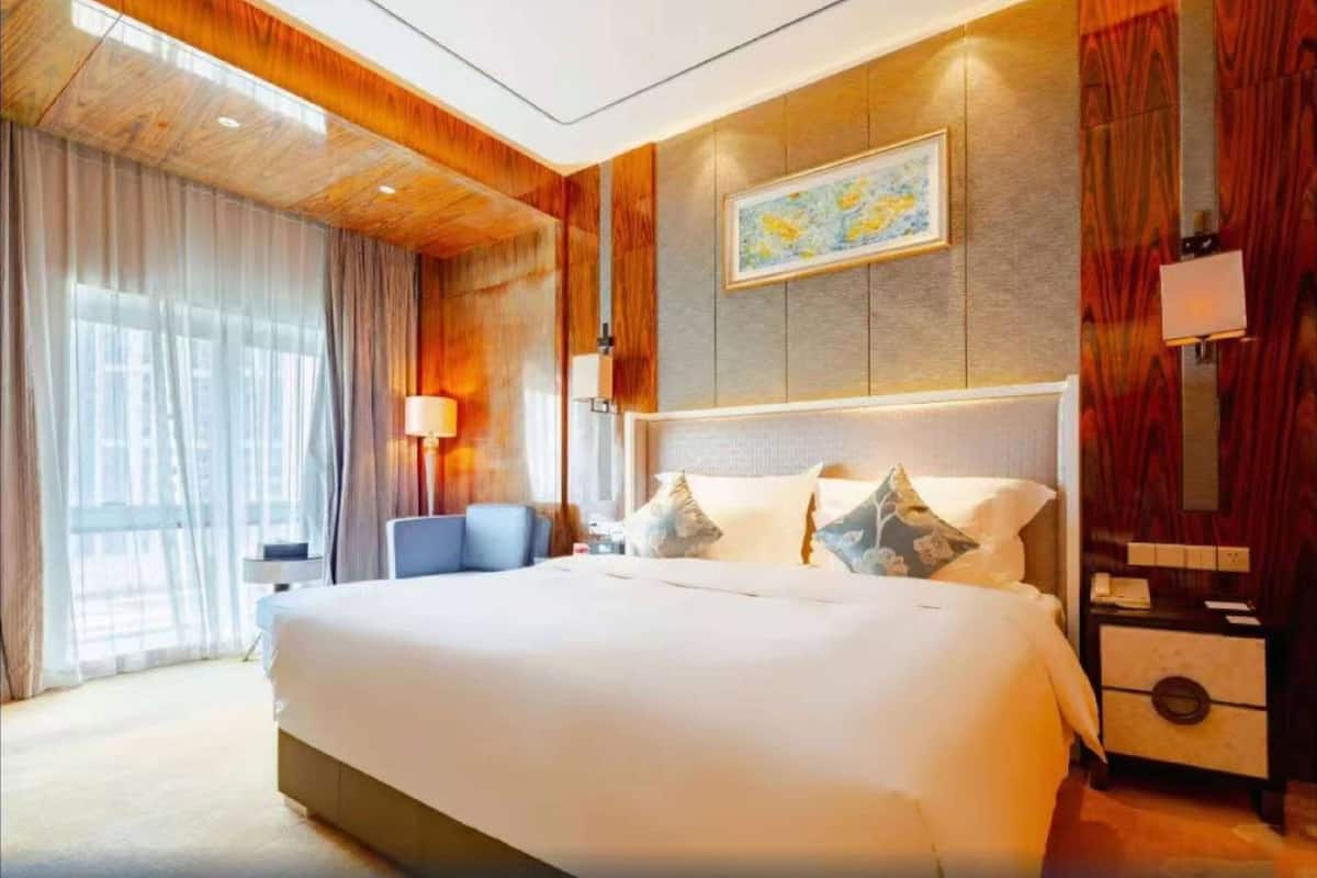 Ein Hotelzimmer mit einem großen Bett, einem Schreibtisch, einem Stuhl und einem Fenster mit Vorhängen.