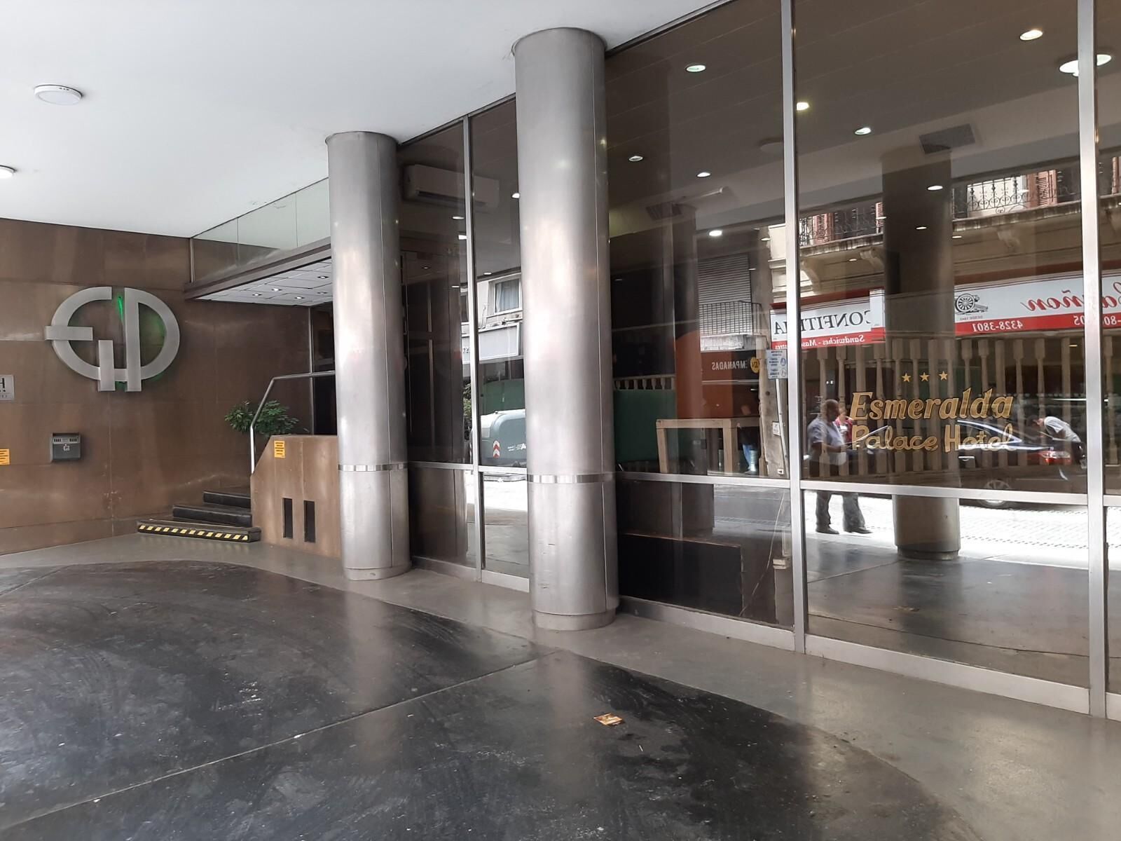 Une entrée moderne avec de grandes portes vitrées, un logo bien visible sur le mur et le reflet d’une enseigne d’hôtel.