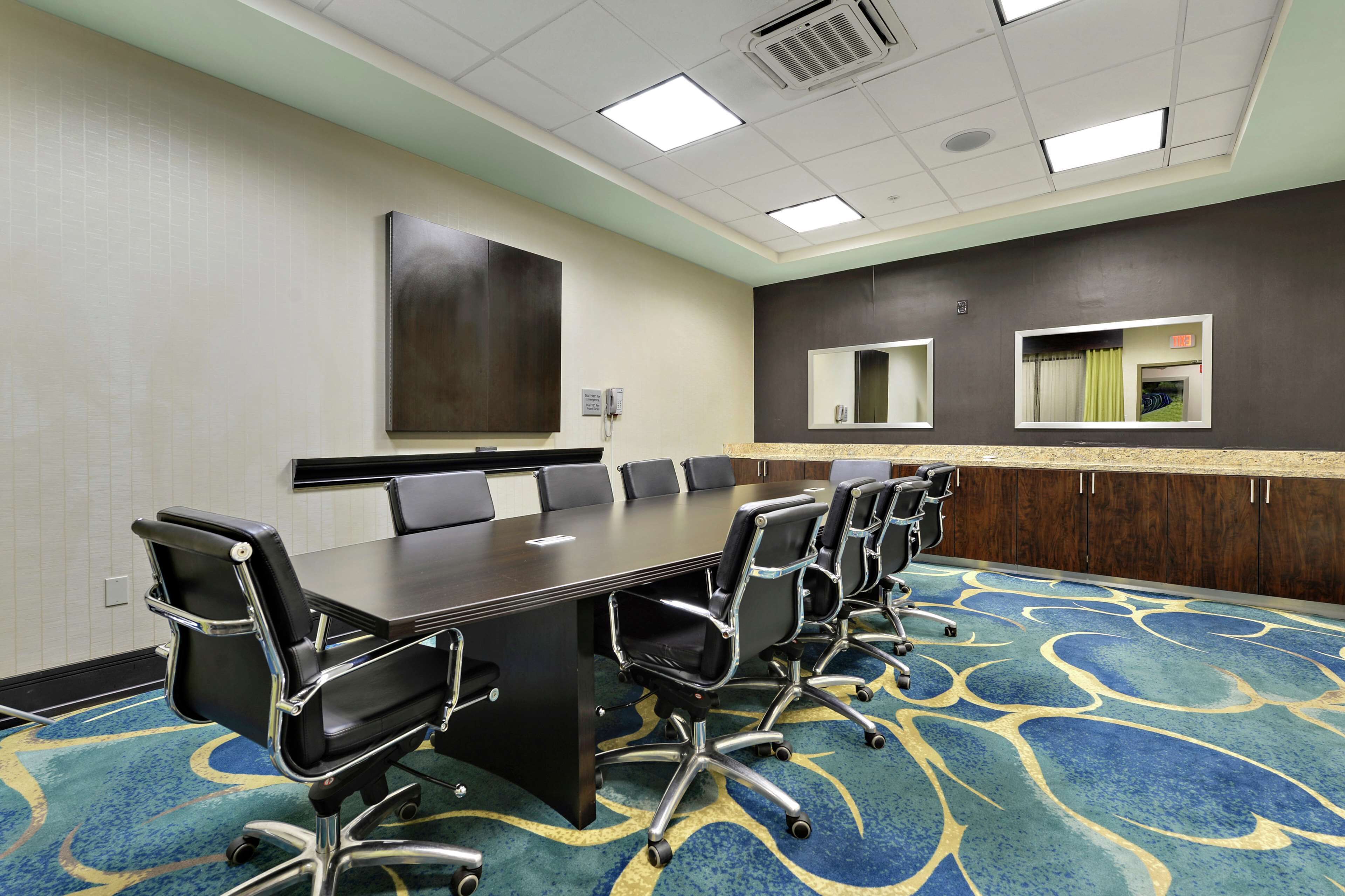 A conference room with a long table, multiple chairs, and a carpeted floor.