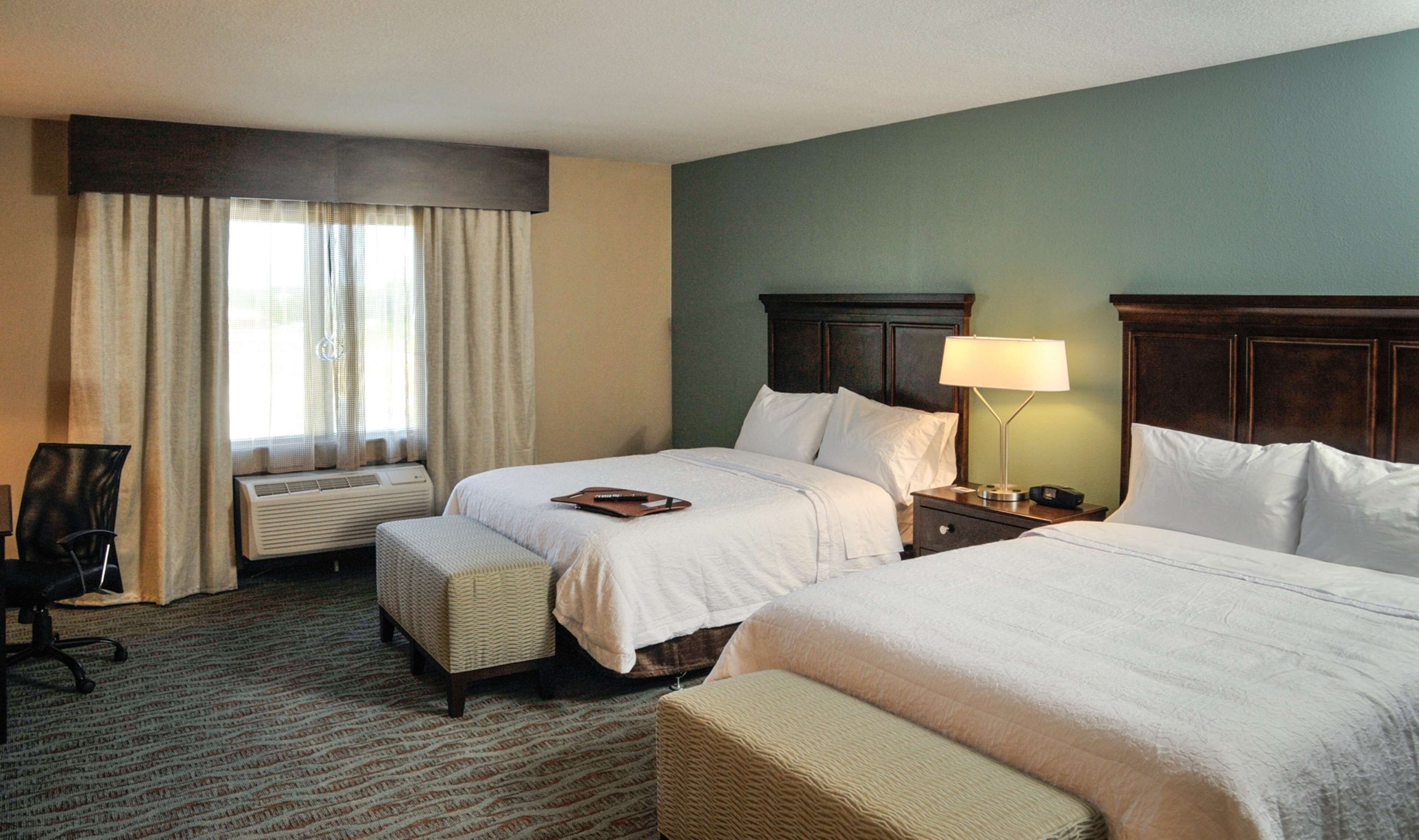 A hotel room with two beds, a desk, a chair, and a window with curtains.
