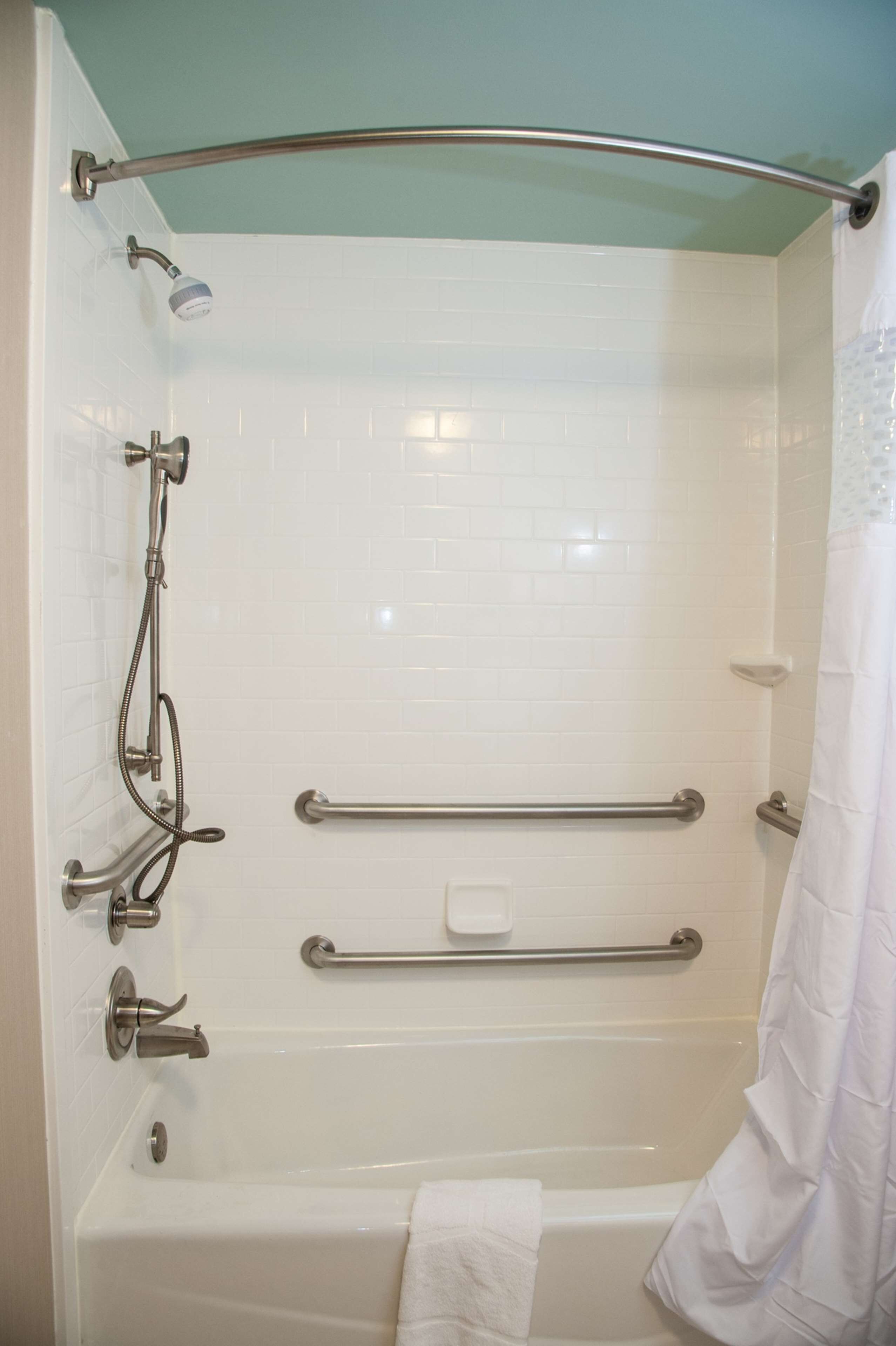 A shower with a grab bar, a handheld showerhead, and a towel rack.