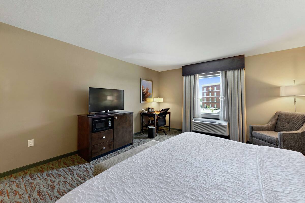 Een hotelkamer met een groot bed, een bureau met stoel, een televisie en een raam met gordijnen.