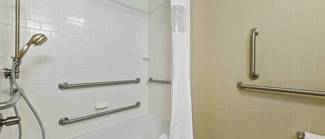 A bathroom with a white bathtub, grab bars, a showerhead, and a toilet.