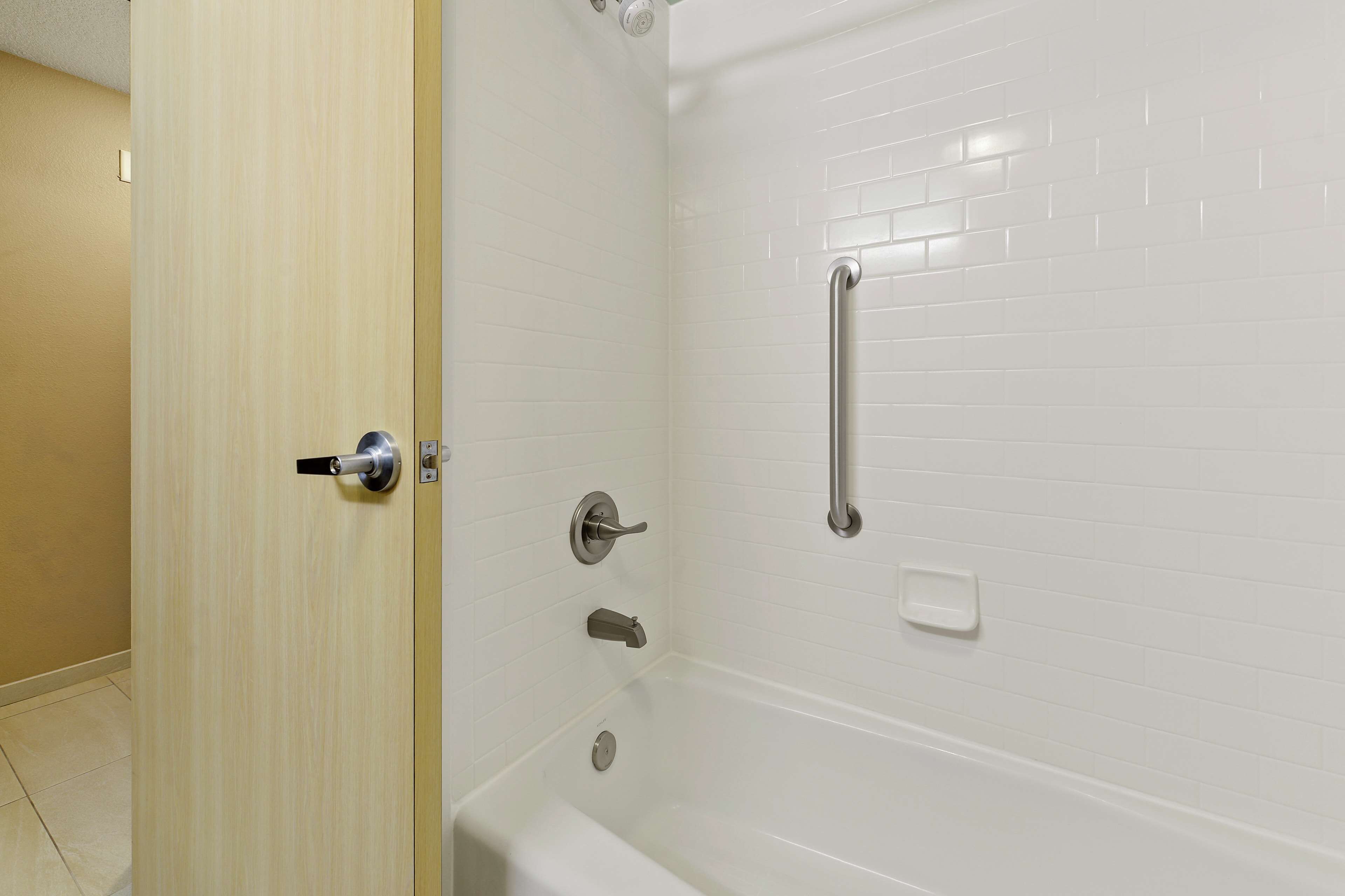 A bathroom with a white bathtub, a handrail, and a door with a handle.
