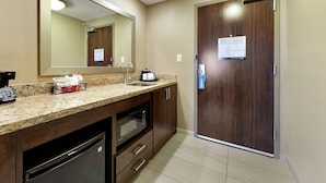 A modern bathroom with a granite countertop, a built-in microwave, a sink, and a wooden door with a sign.