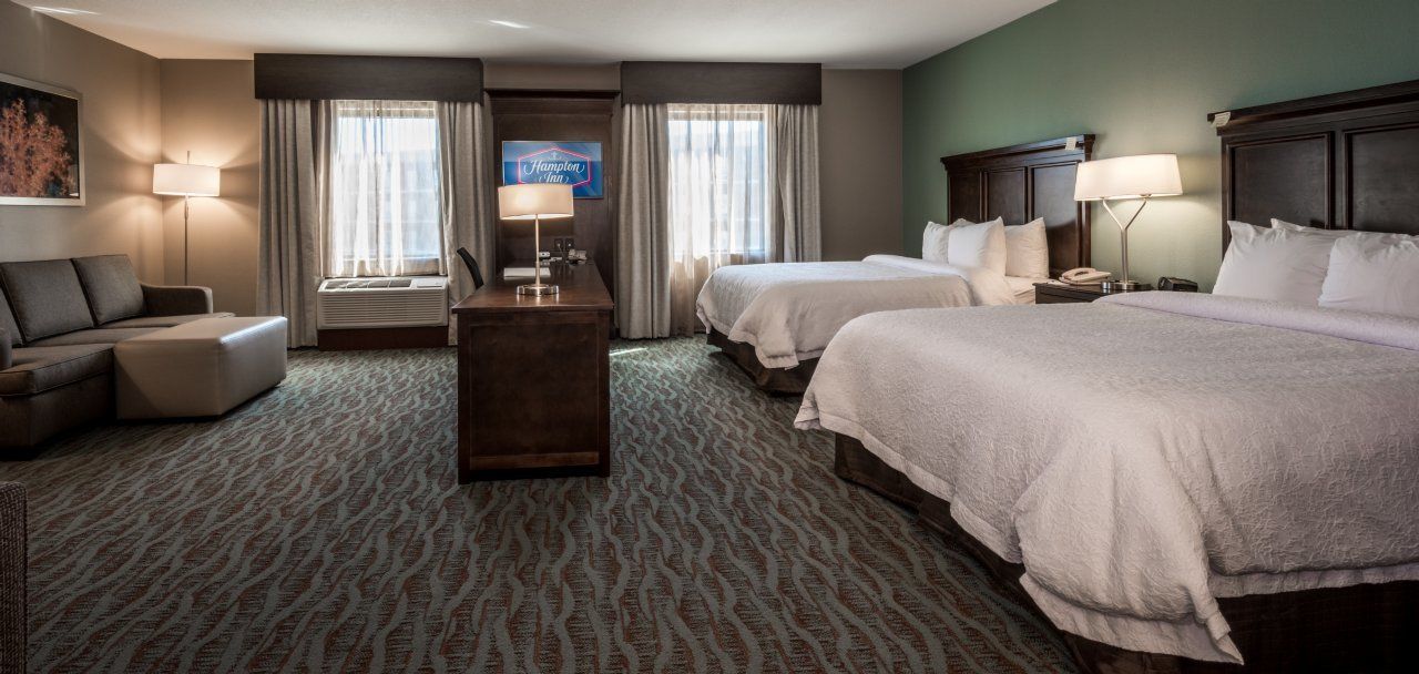A hotel room with two beds, a sofa, a desk, and a TV.