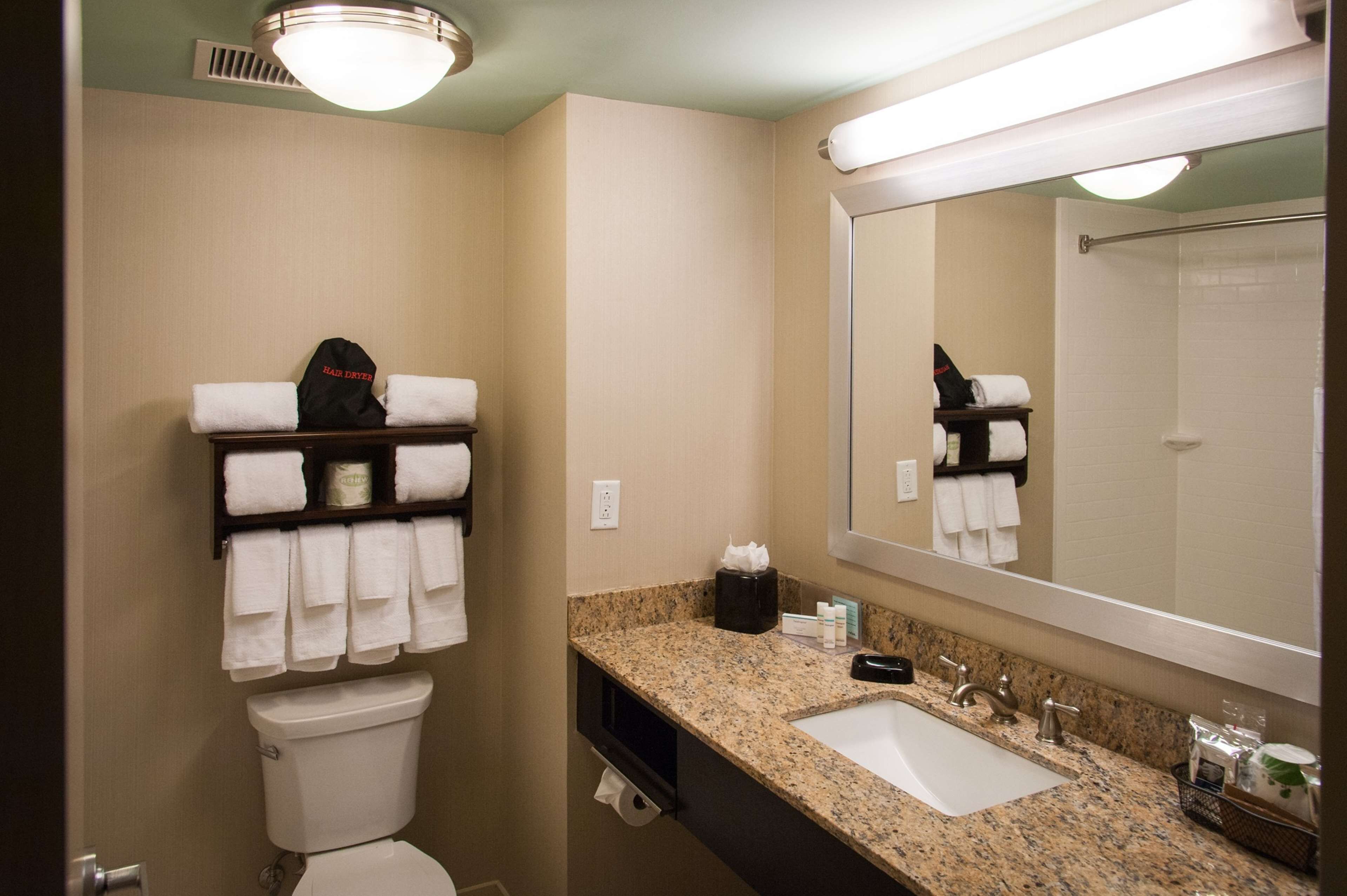 Ein Badezimmer in einem Hotel mit Toilette, Waschbecken und Spiegel. Auf der Ablage liegen Handtücher und Pflegeprodukte.