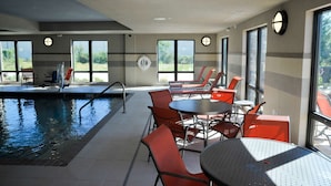 A pool area with chairs and tables, large windows, and a ceiling with recessed lighting.