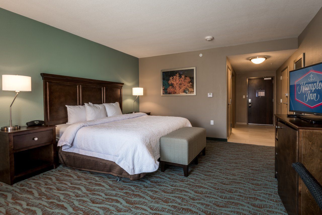 A hotel room with a large bed, a nightstand, a lamp, a television, and a framed picture on the wall.