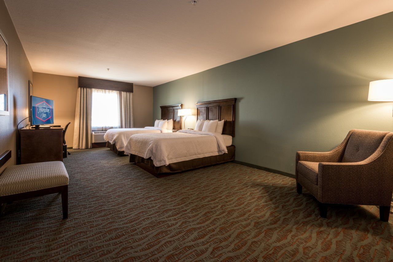 A hotel room with two beds, a desk, a chair, and a television.