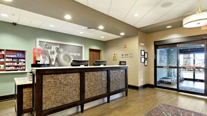 A hotel reception area with a reception desk, a seating area, and a view of the outside through a glass door.