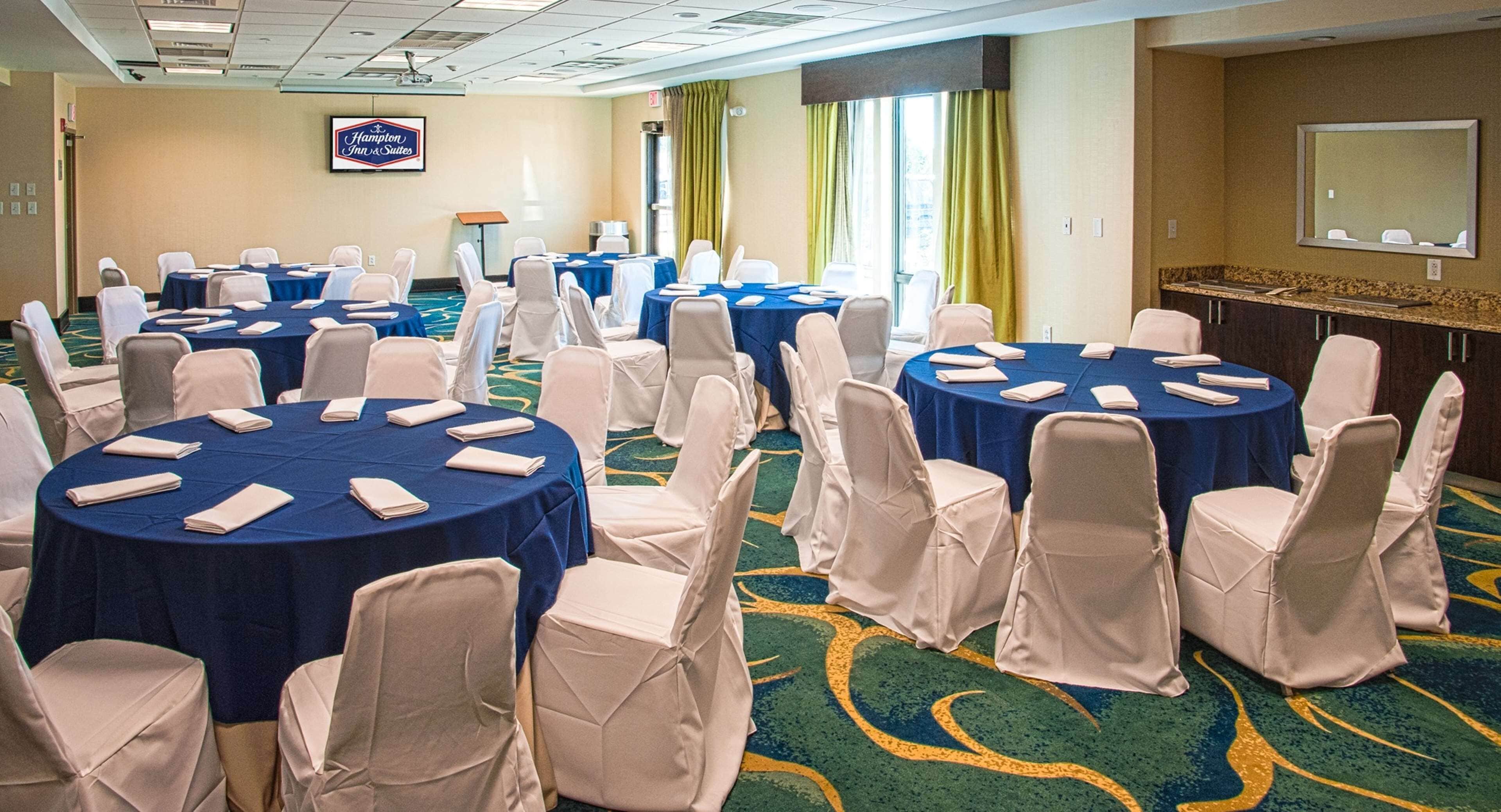 A conference room with multiple round tables, each with white chairs and blue tablecloths.
