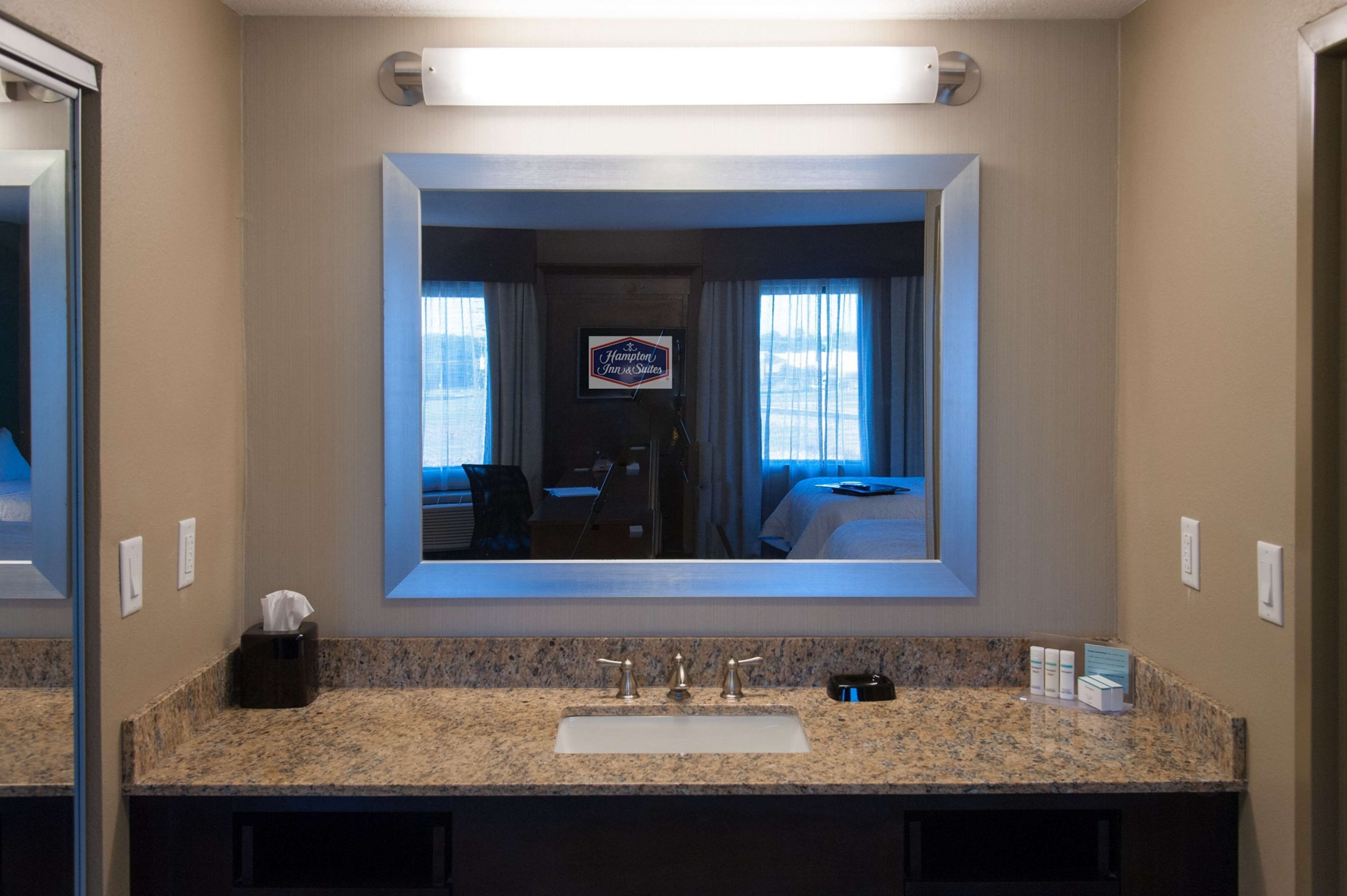 A hotel bathroom with a large mirror, granite countertop, and a sink.