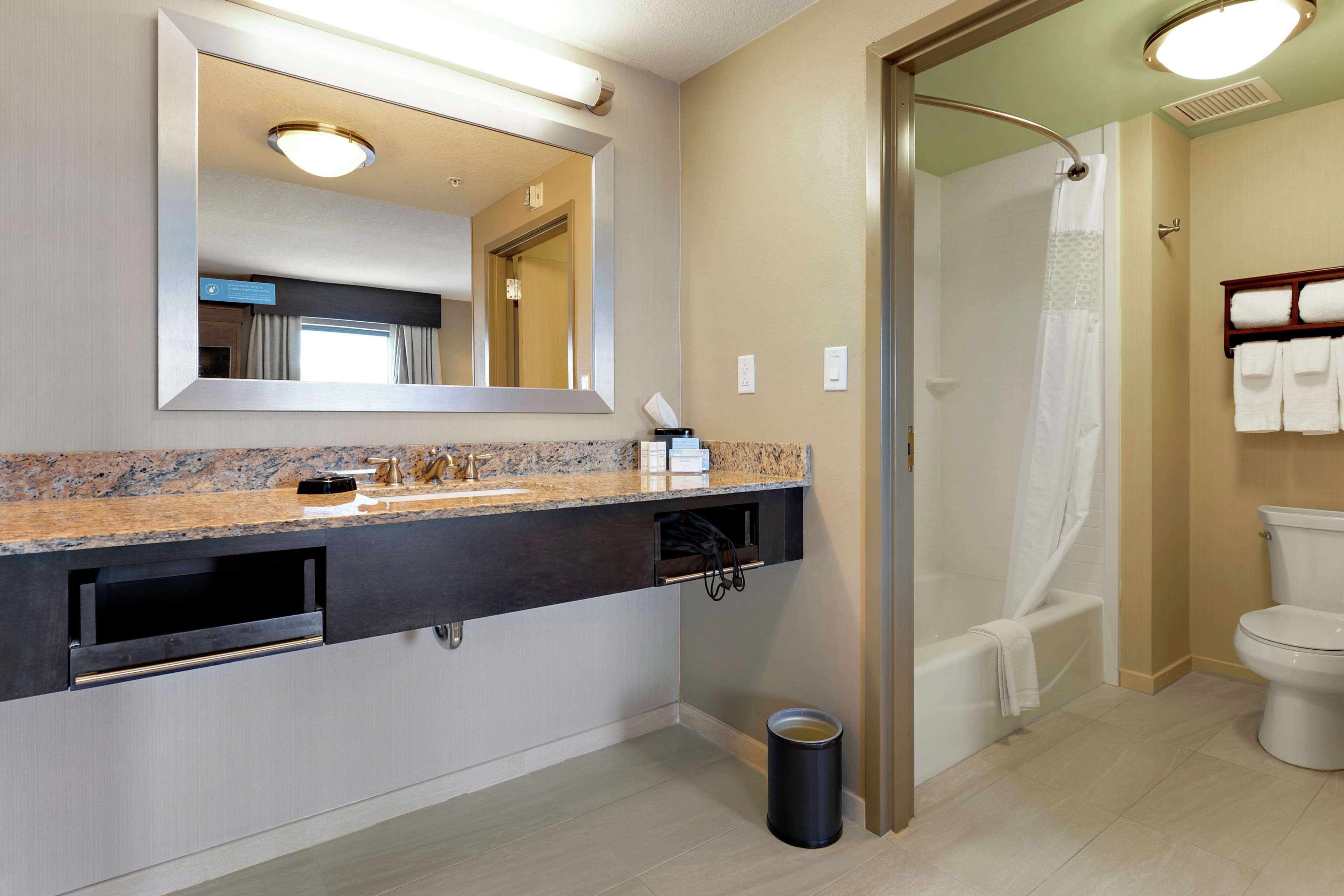 Un baño moderno con encimera de granito, un espejo grande, una ducha con puerta de vidrio y un inodoro.